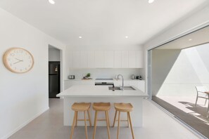 Une cuisine moderne avec un îlot central, des tabourets de bar, une horloge et une vue sur l’extérieur grâce à une porte vitrée.