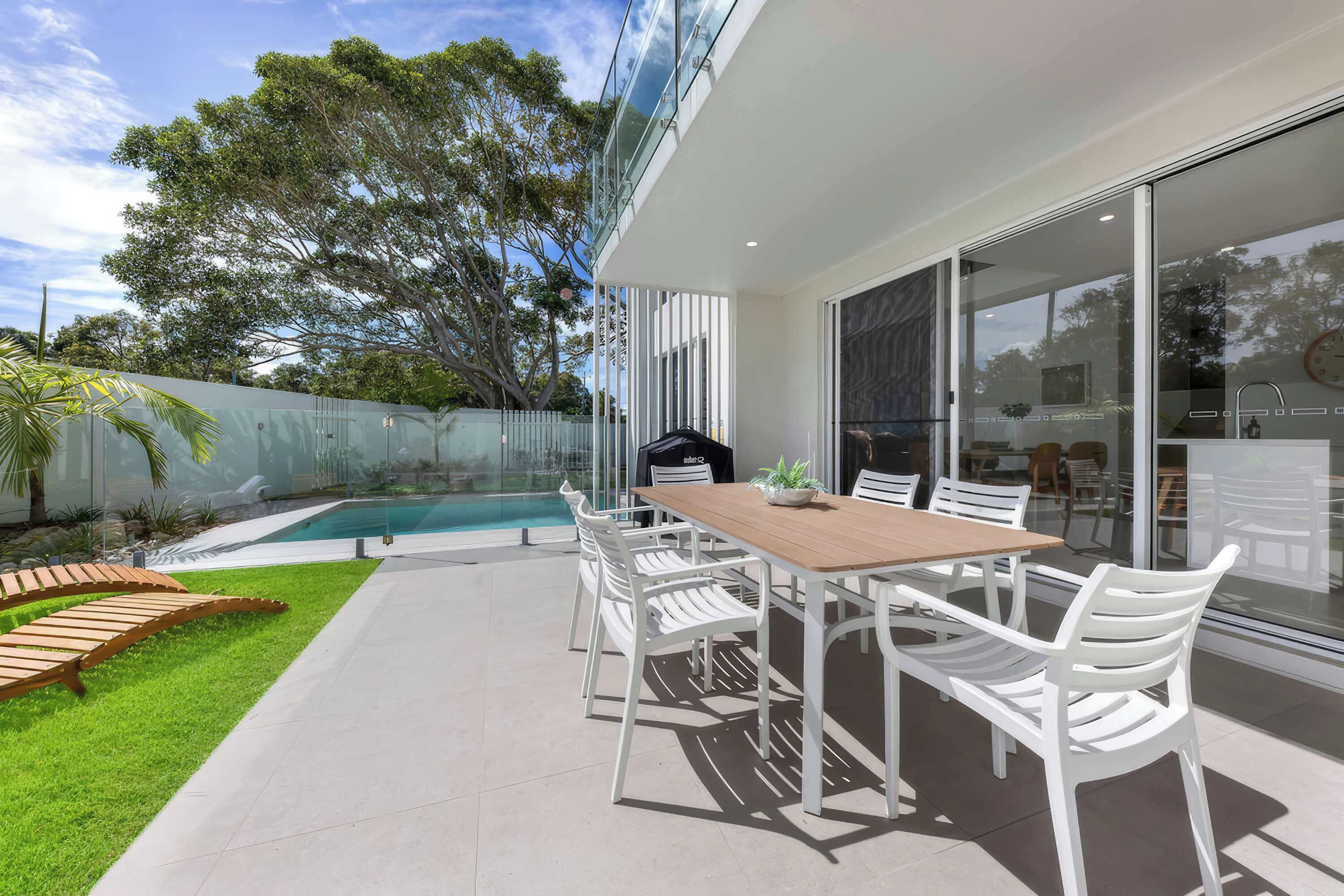 A modern outdoor dining area with a pool, white chairs, and a glass-enclosed space.