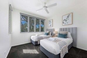 Une chambre avec deux lits, un ventilateur de plafond et une grande fenêtre donnant sur les arbres.
