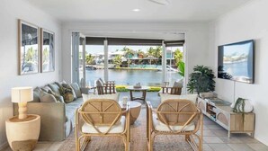 Un salon moderne avec vue sur une piscine et des palmiers, des meubles en osier et un téléviseur à écran plat.