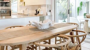 Une cuisine moderne avec des meubles blancs, un îlot central et un coin repas comprenant une table en bois et des chaises en osier.