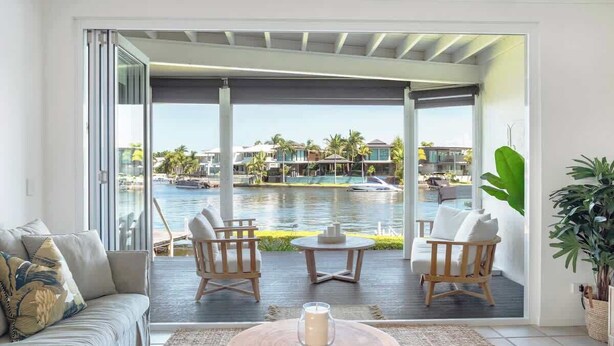 Un salon moderne avec vue sur un port de plaisance, comprenant un canapé, deux fauteuils, une table basse et une plante en pot.