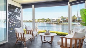 Une terrasse en bois avec des sièges extérieurs, une vue sur une étendue d’eau et, au loin, une côte bordée de bâtiments.