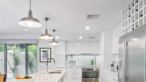 Cozinha moderna com armários brancos, eletrodomésticos de aço inoxidável e iluminação pendente.
