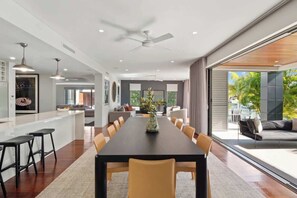 A modern dining area with a long table, chairs, and a ceiling fan. - Exclusive Waterfront Oasis w/ Private Beach & Pool (Noosa Region)