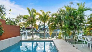 Piscina com vista para um porto, cercada por palmeiras e um cercado de madeira.
