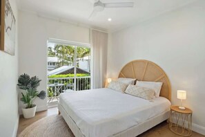 Ein Schlafzimmer mit einem großen Bett, einem Deckenventilator, einer Topfpflanze und Blick ins Freie.