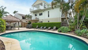 A swimming pool with lounge chairs, a thatched umbrella, and a building with balconies. - Modern, Stylish, Resort style Noosa River stay (Noosa Region)