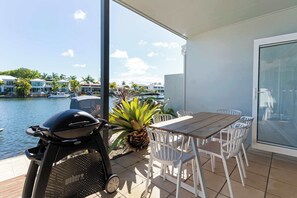 Un balcón con una parrilla, una mesa de comedor, sillas y vista a un puerto deportivo.