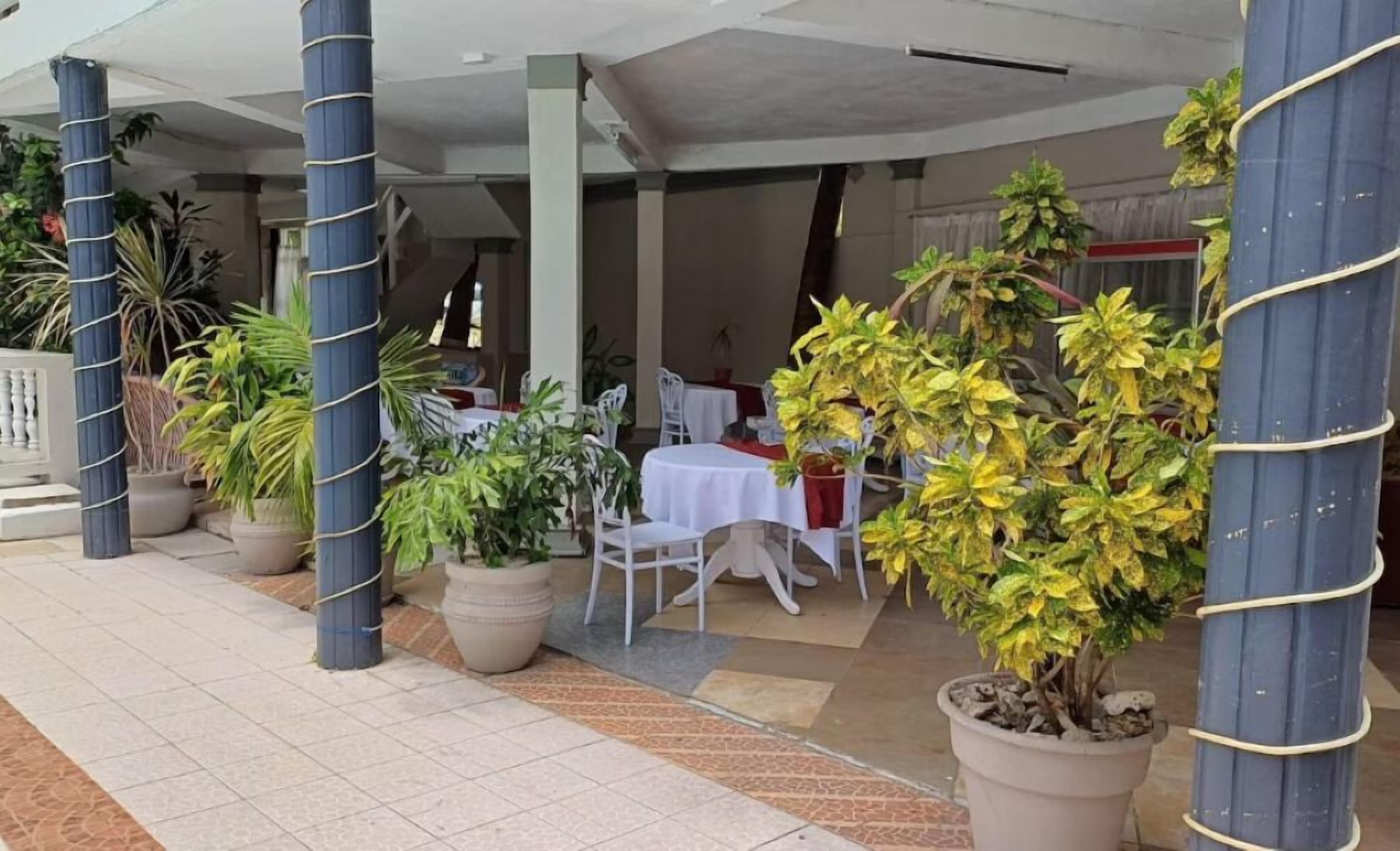 An outdoor dining area with potted plants, white tables, and chairs.