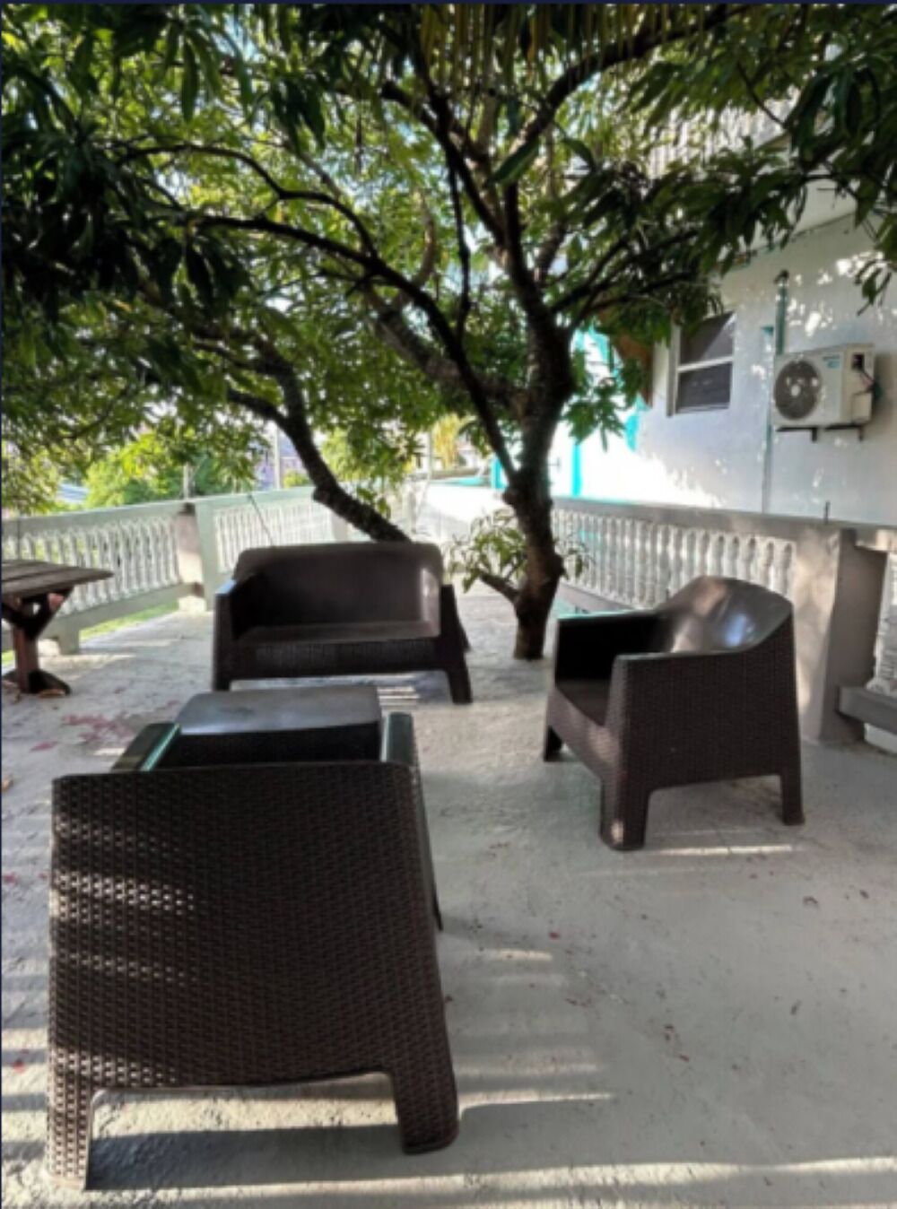 Un espace extérieur aménagé avec des meubles en osier, un arbre et un bâtiment doté d’un appareil de climatisation.