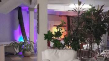 A spacious room with a white tiled floor, a white sofa, and potted plants.