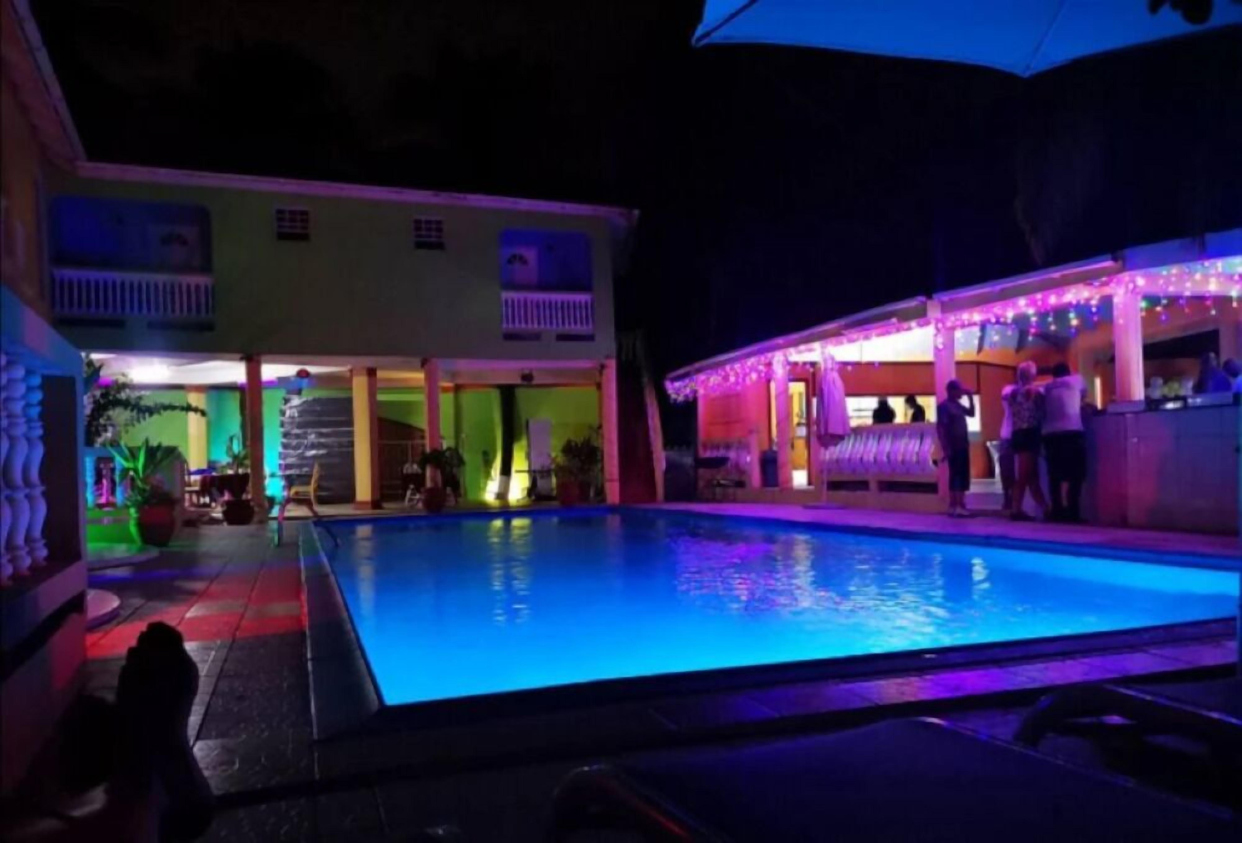 A swimming pool with a view of a building with balconies and a bar area with people.