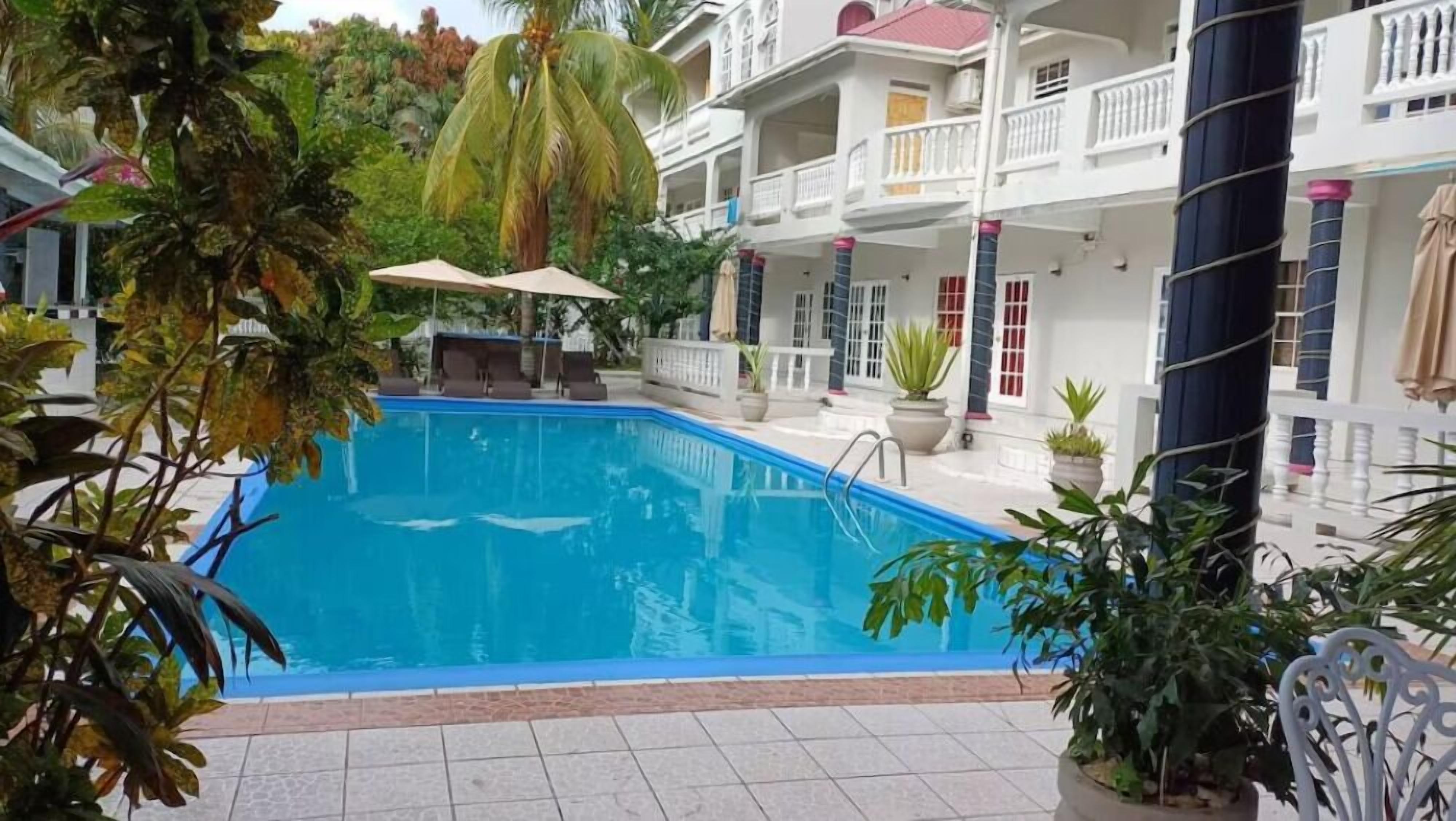 Piscina rodeada por plantas em vasos e um edifício branco com varandas.
