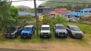 A row of parked cars on a grassy area with houses and greenery in the background. - Cozy 1-Bdrm Studio in Rodney Bay with AC (Gros Islet)