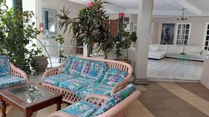 Un vaste espace de vie agrĂ©mentĂ© de meubles en osier, dâune table basse en verre et de plusieurs plantes en pot.