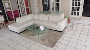 Una sala de estar con un sofá sectional blanco, una mesa de centro de vidrio y piso de baldosas.