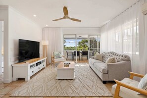 Ein modernes Wohnzimmer mit Flachbildfernseher, einer Couch, einem Couchtisch und einem Deckenventilator.