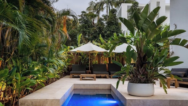 Un área de piscina con sillones de descanso y sombrillas, rodeada de exuberante vegetación tropical.