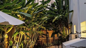 Un patio con un camino de piedra, un banco y abundante vegetación.