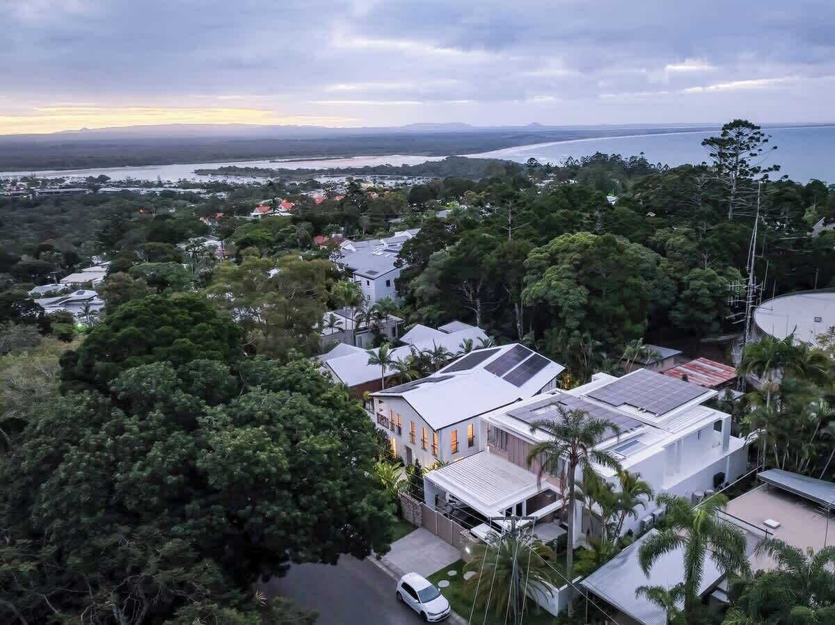 Un quartier résidentiel où les maisons sont entourées d’une végétation luxuriante, avec une rivière en arrière-plan et un ciel dégagé.
