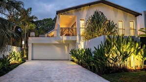 Una casa moderna de dos pisos con garaje, rodeada de plantas tropicales.