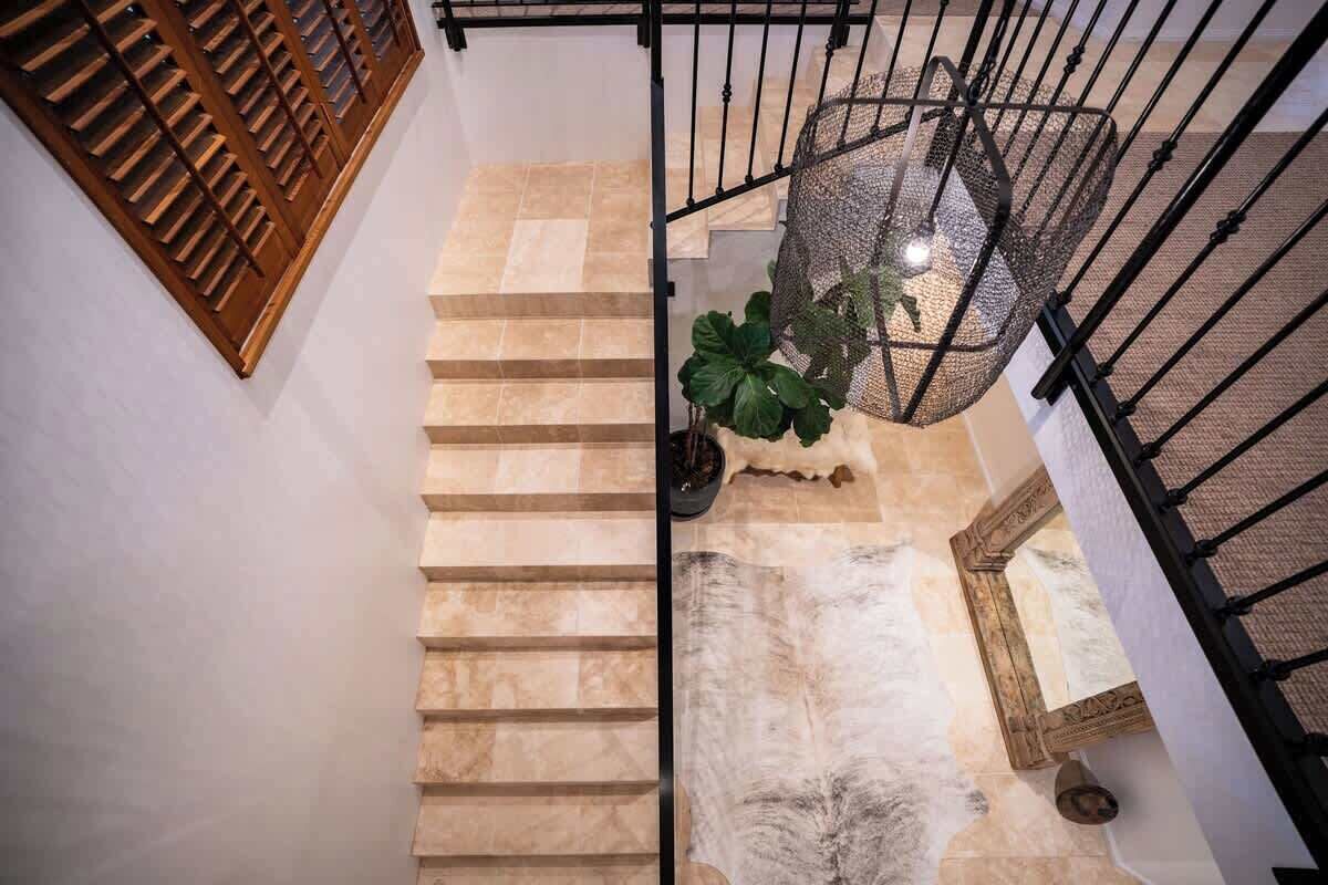 A staircase with beige steps, a black metal railing, a hanging light fixture, and a potted plant.