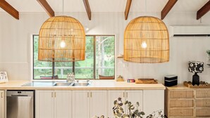 A modern kitchen with two large, woven pendant lights, a stainless steel dishwasher, and a large window with a view of greenery.