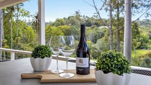 A table with a wine bottle, two glasses, and two potted plants on a balcony with a scenic view.