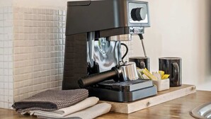 En kaffemaskin står på en bänkskiva, bredvid finns ett bricka, en trasa och en mugg.