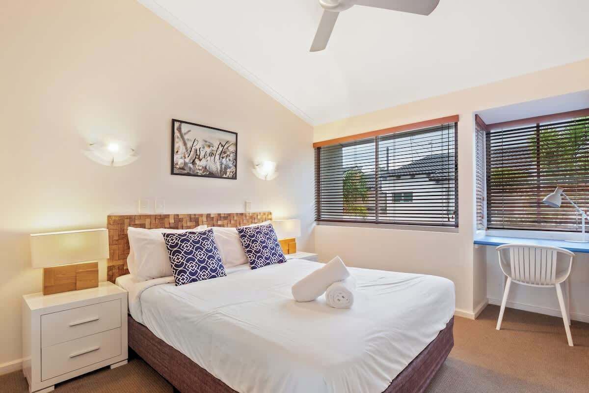 Quarto com cama, mesas de cabeceira, escrivaninha e uma cadeira.