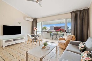 A modern living room with a flat-screen TV, a dining area, and a balcony with a view. - Prime Noosa Location with Pool (Noosa Region)