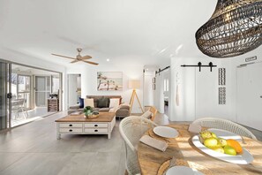 A modern living room with a dining table set, a sofa, and a ceiling fan. - Sandy Daze - Noosa Sound Canalfront Apartment (Noosa Region)