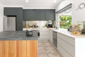 Une cuisine moderne dotée d’un îlot central, d’appareils électroménagers intégrés et offrant une vue sur la verdure environnante.