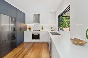 A modern kitchen with a built-in oven, a stainless steel refrigerator, and a large window. - Ultimate Sunshine Beach Pad, Pet Friendly + Pool (Noosa Region)