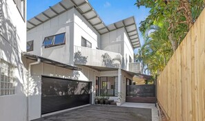 A modern two-story building with a garage, a wooden fence, and potted plants. - Ultimate Sunshine Beach Pad, Pet Friendly + Pool (Noosa Region)