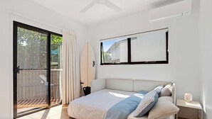 Een slaapkamer met een bed, een raam, een plafondventilator en een schuifdeur van glas die naar een buitengebied leidt.
