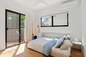 A bedroom with a bed, a window, a ceiling fan, and a sliding glass door leading to an outdoor area. - Ultimate Sunshine Beach Pad, Pet Friendly + Pool (Noosa Region)