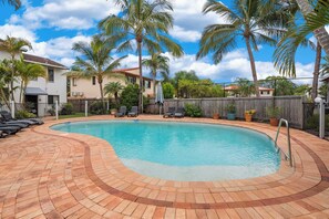 A swimming pool with a brick deck, surrounded by palm trees and a wooden fence. - Modern Noosaville Townhouse - Pool, Tennis, River (Noosa Region)