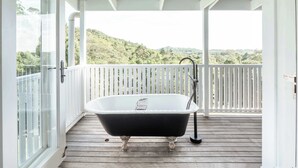 A freestanding bathtub on a wooden deck with a white railing, overlooking a forested hillside. - Little Red Barn in the Noosa Hinterland (Hinterland Region)