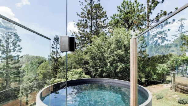 A glass-enclosed hot tub with a clear view of surrounding trees and a wooden deck. - Little Red Barn in the Noosa Hinterland (Hinterland Region)