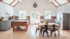 A spacious kitchen with wooden beams, a central island, and a dining area with chairs. - Little Red Barn in the Noosa Hinterland (Hinterland Region)