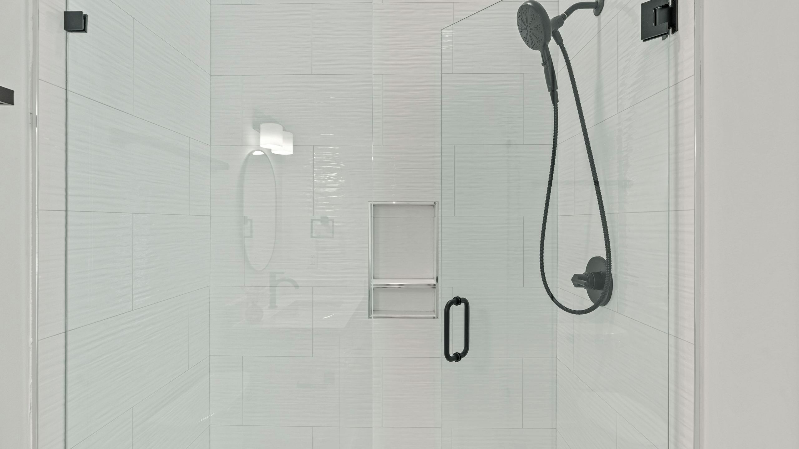 Une salle de bain moderne avec une douche à parois de verre, une douchette à main, un robinet mural et une petite étagère.