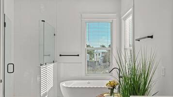 Une salle de bain moderne dotée d’une douche à parois de verre, d’une baignoire sur pieds et d’une fenêtre avec stores.