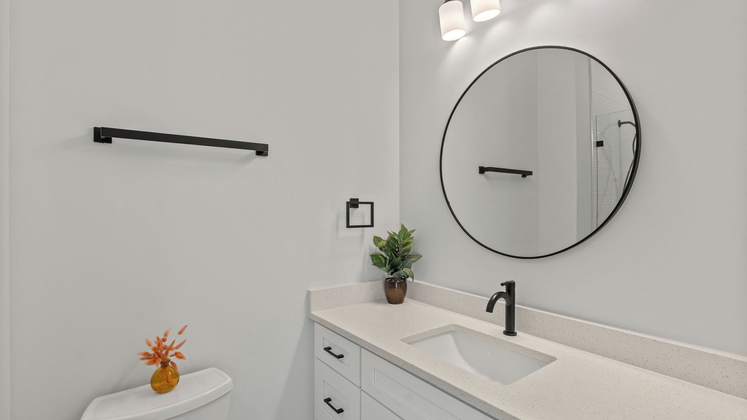 A modern bathroom with a white sink, a round mirror, a towel rack, a potted plant, and a toilet.