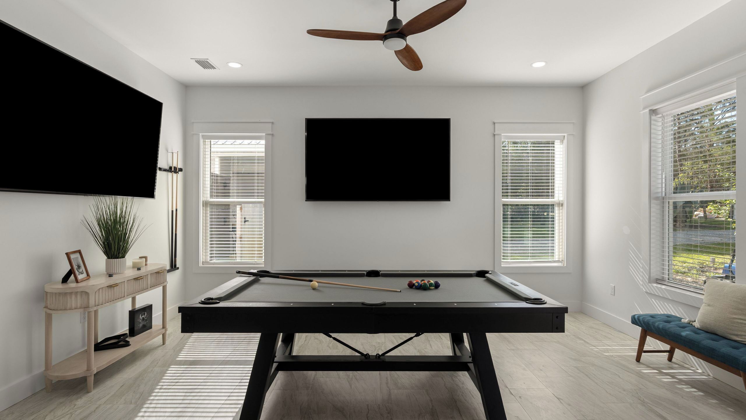 A pool table with a ceiling fan, a mounted TV, and a window with blinds.