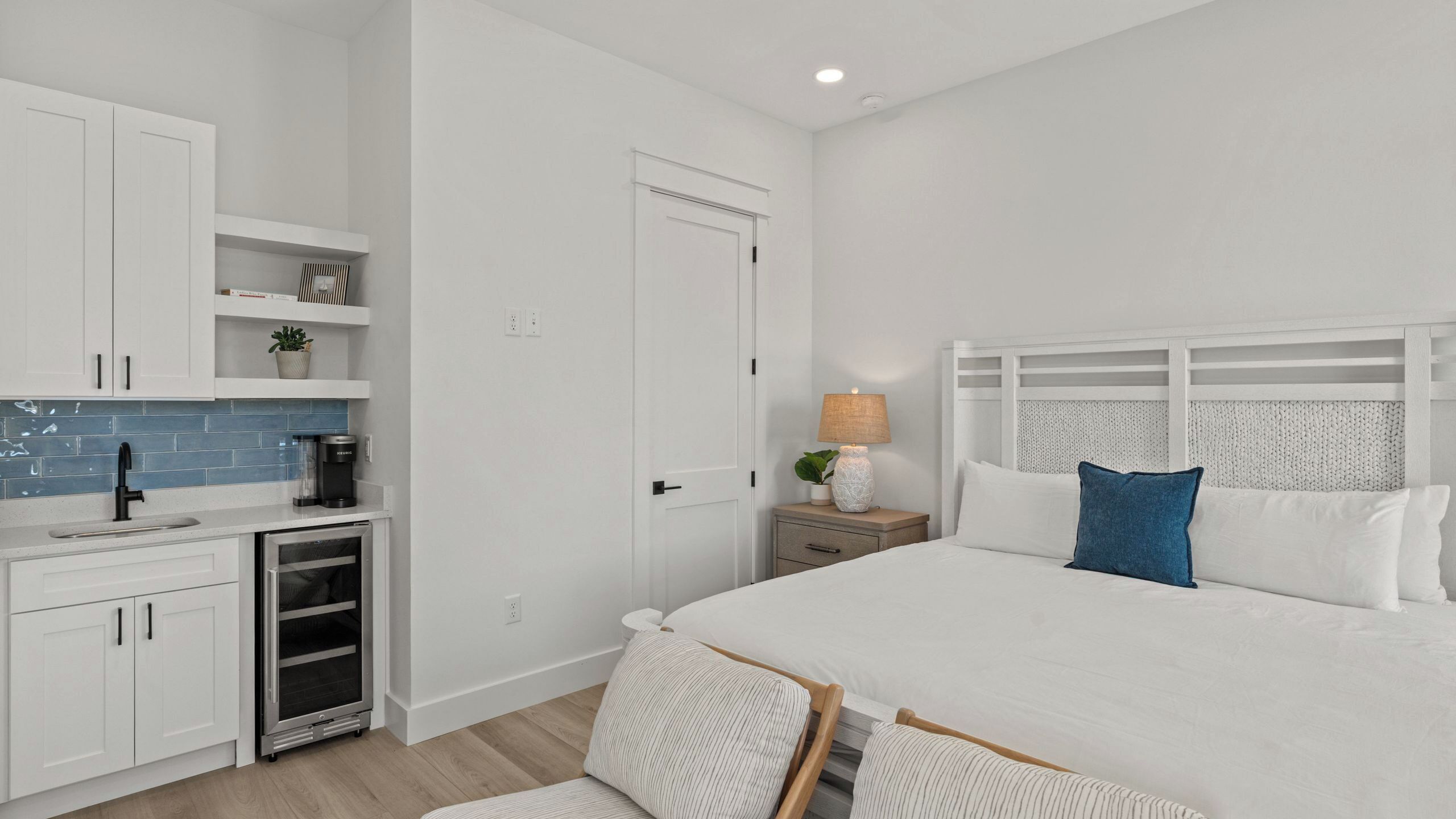 Un dormitorio con cama, mesita de noche, lámpara y una pequeña kitchenette con cafetera.