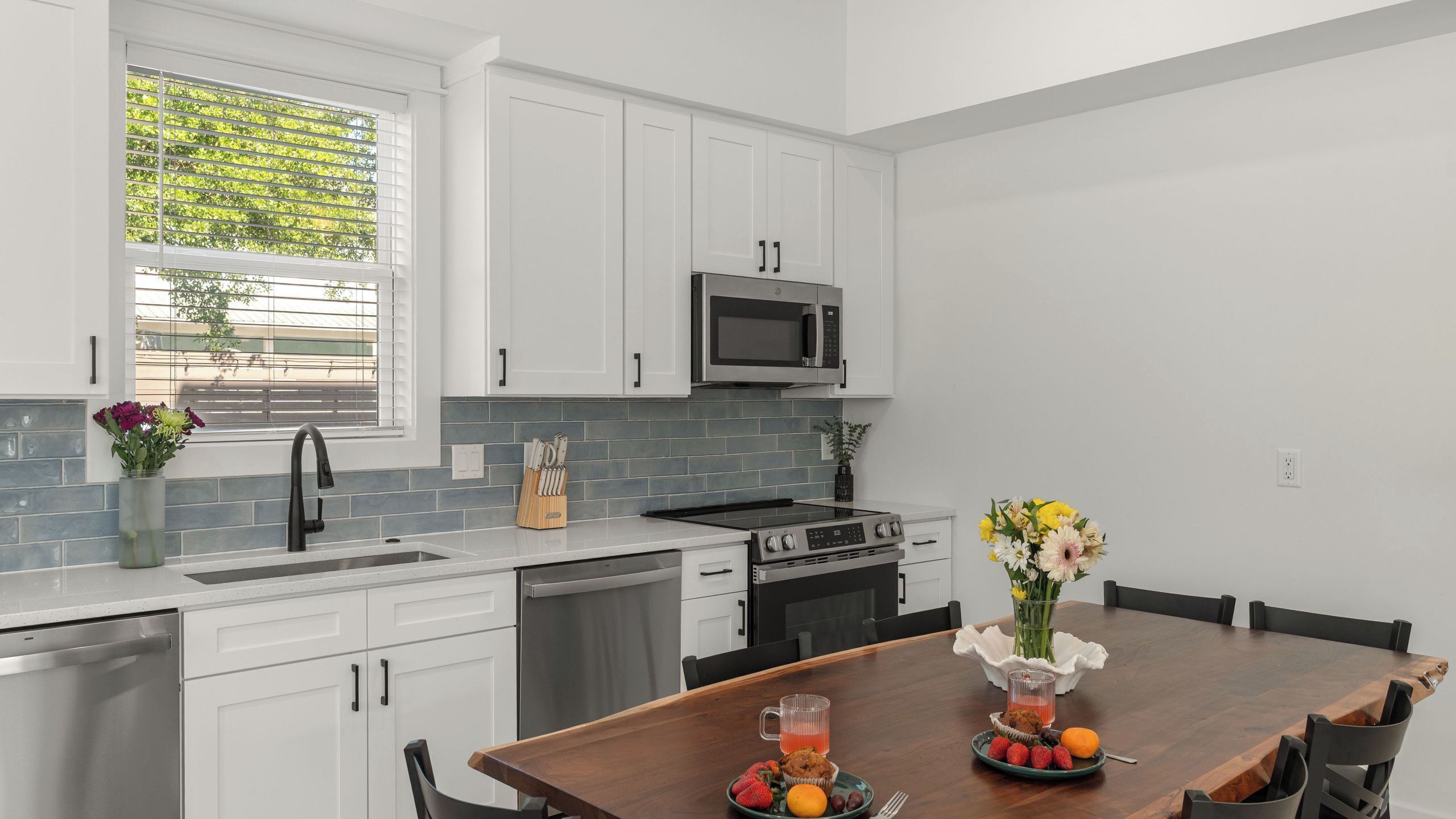 A modern kitchen with white cabinets, a microwave, a dishwasher, and a dining area with a table set for two.