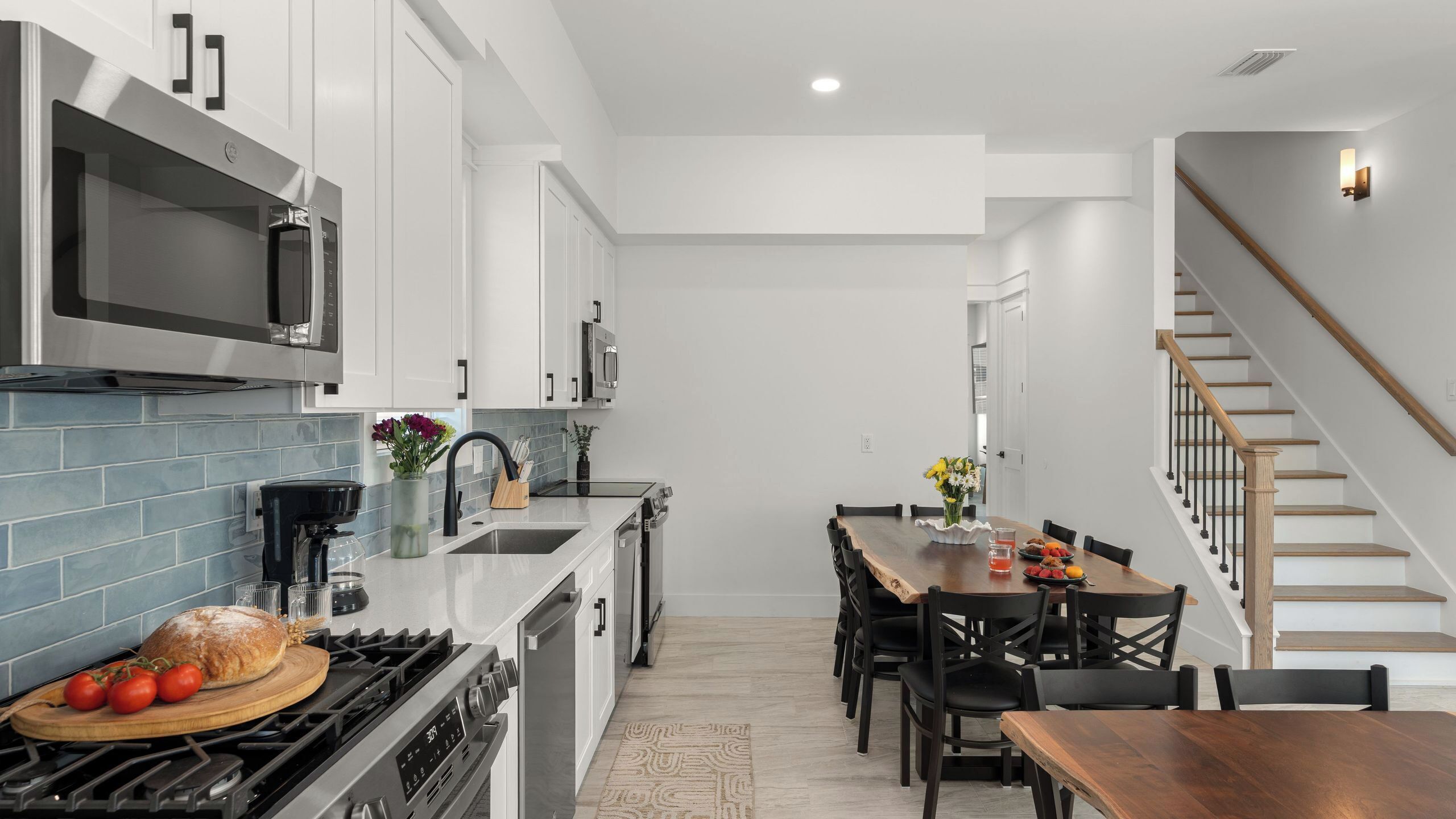 Una cocina moderna con armarios blancos, un microondas y una estufa. Hay un comedor con una mesa y sillas de madera.