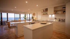 Una cocina moderna con una isla grande, armarios blancos y vista al mar.